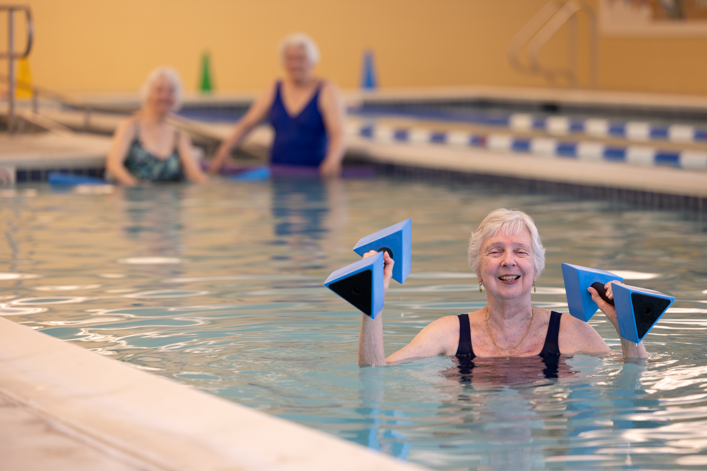 Senior woman doing water aerobics with foam weights