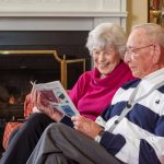 A couple enjoys reading the newspaper in front of a fireplace
