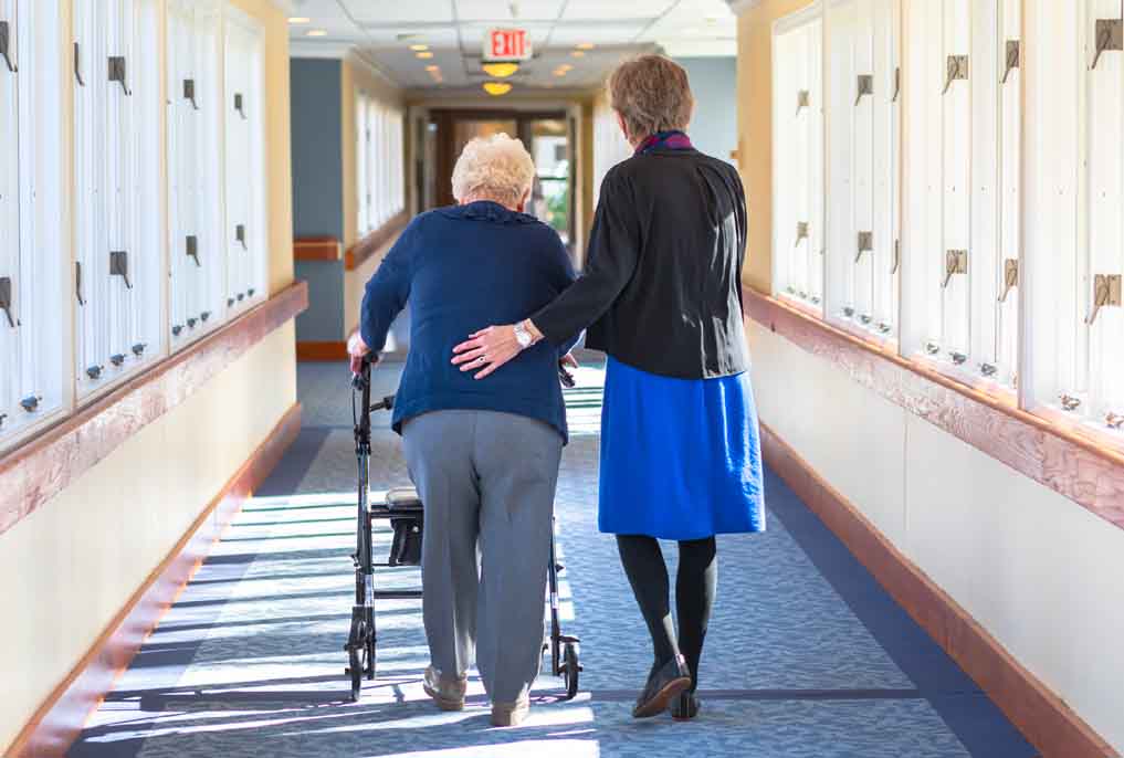 A resident with a walker is assisted by her daughter