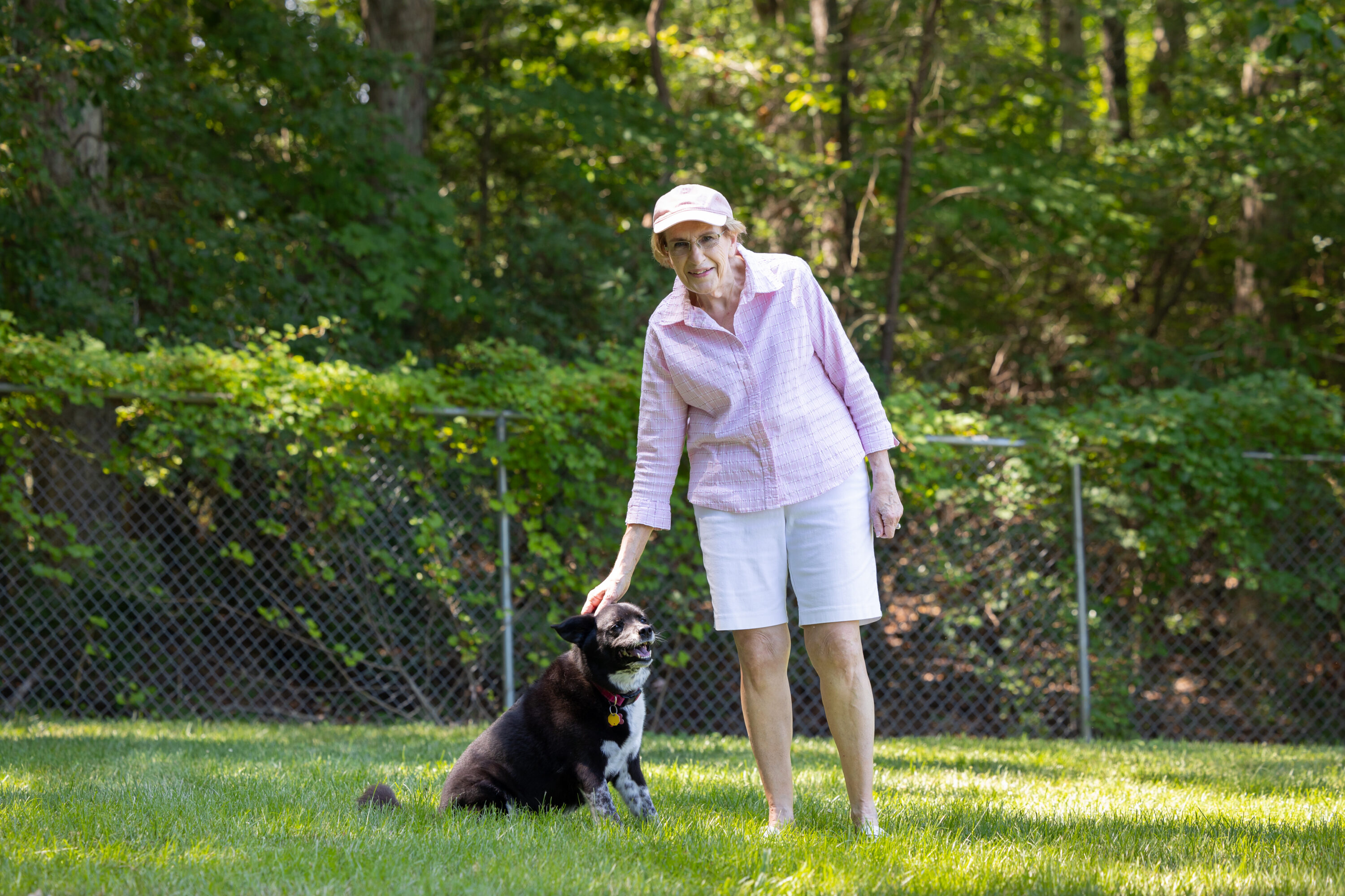 Woman petting black dog in grassy yard