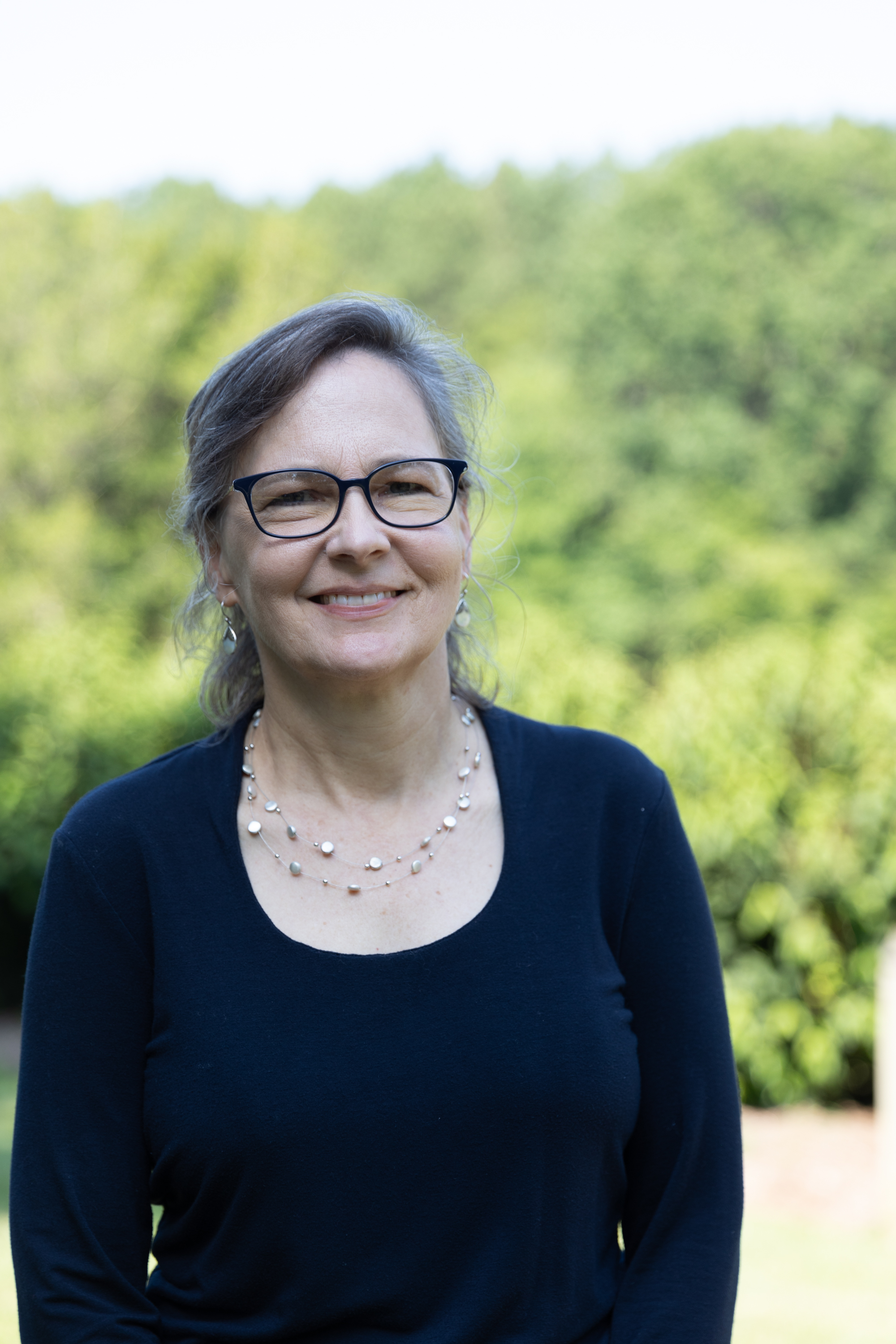 Smiling woman with glasses outdoors against green trees