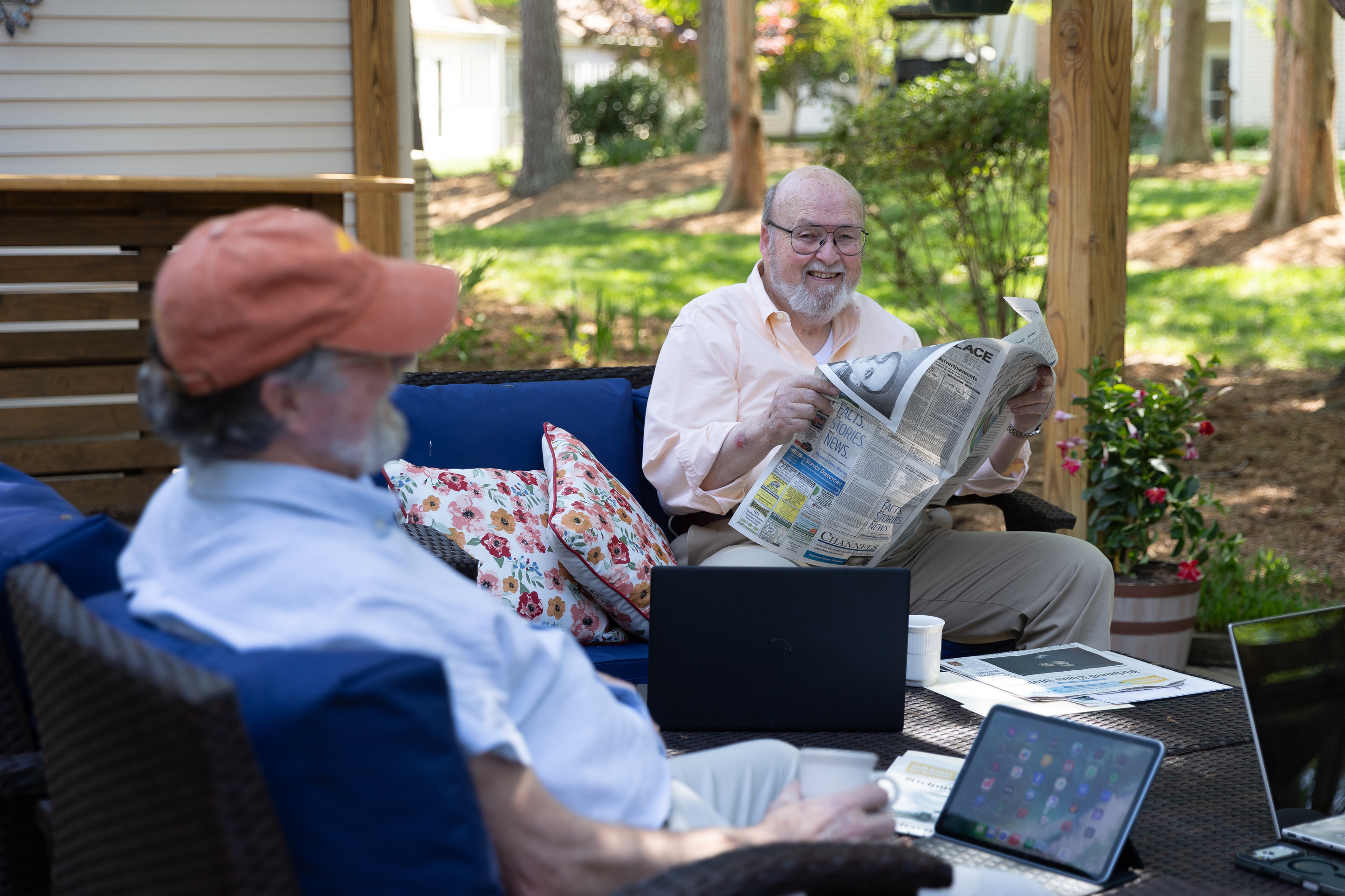 Two elderly men reading newspaper and using tablet outdoors