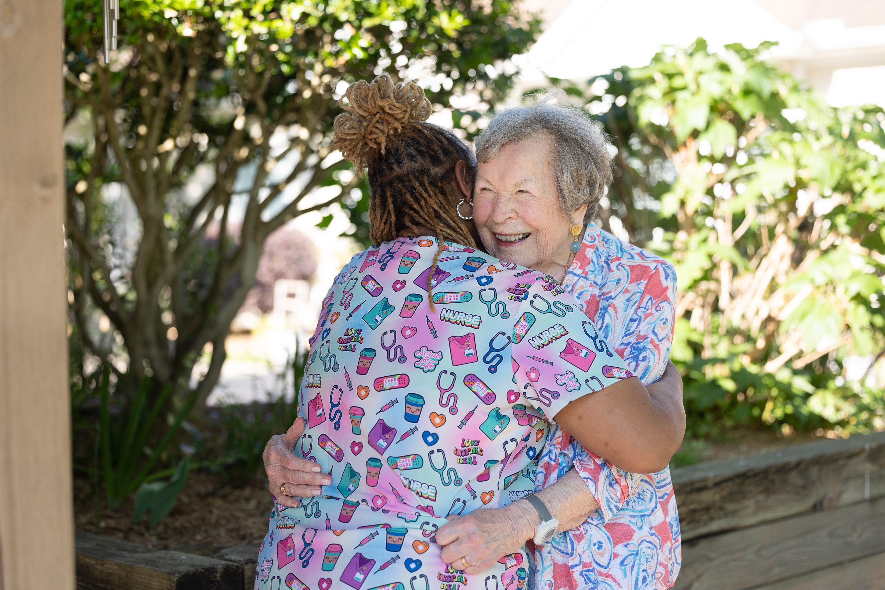 Elderly woman hugging caregiver outdoors in garden