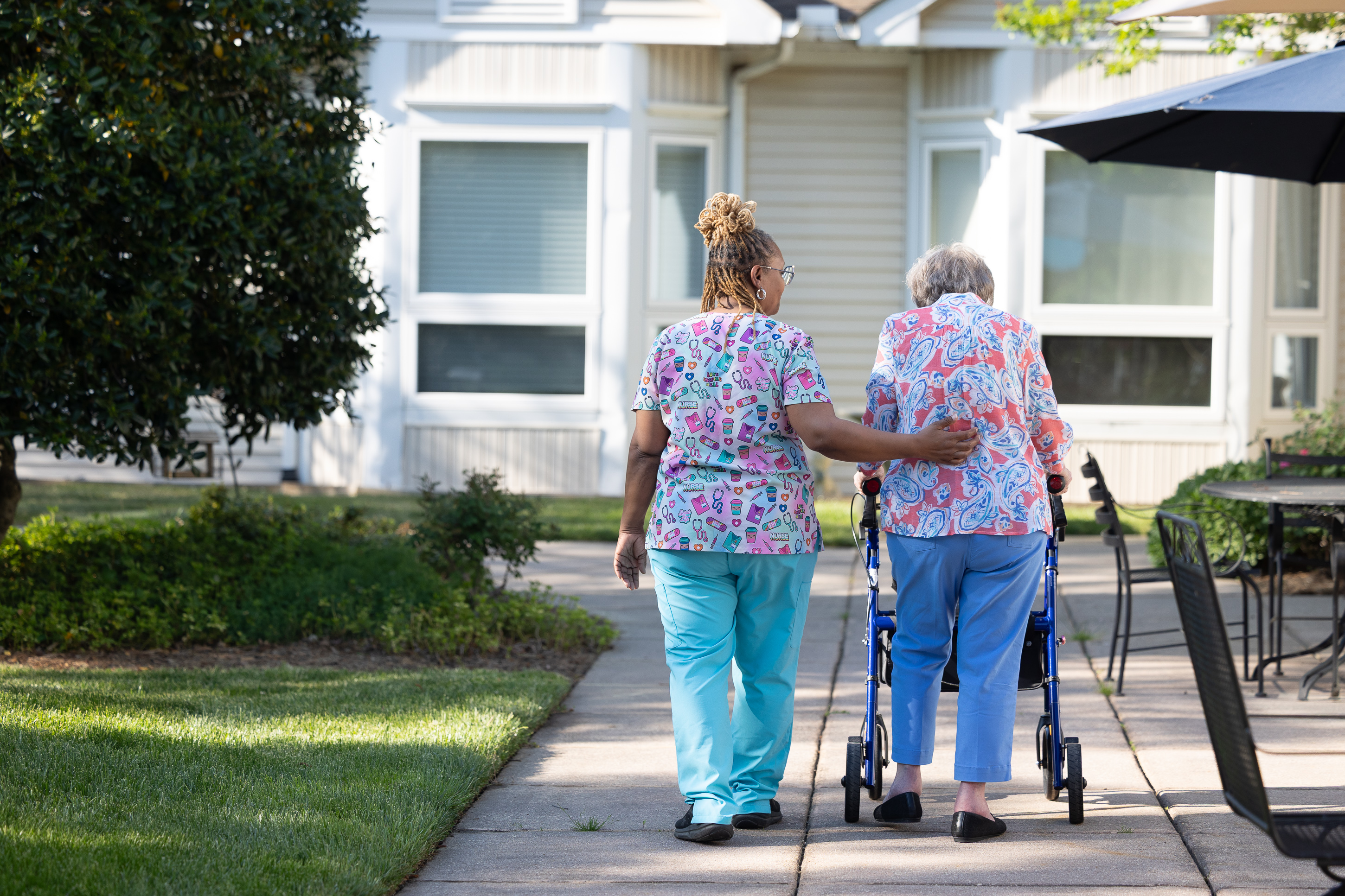 Caregiver assisting elderly woman with walker outdoors