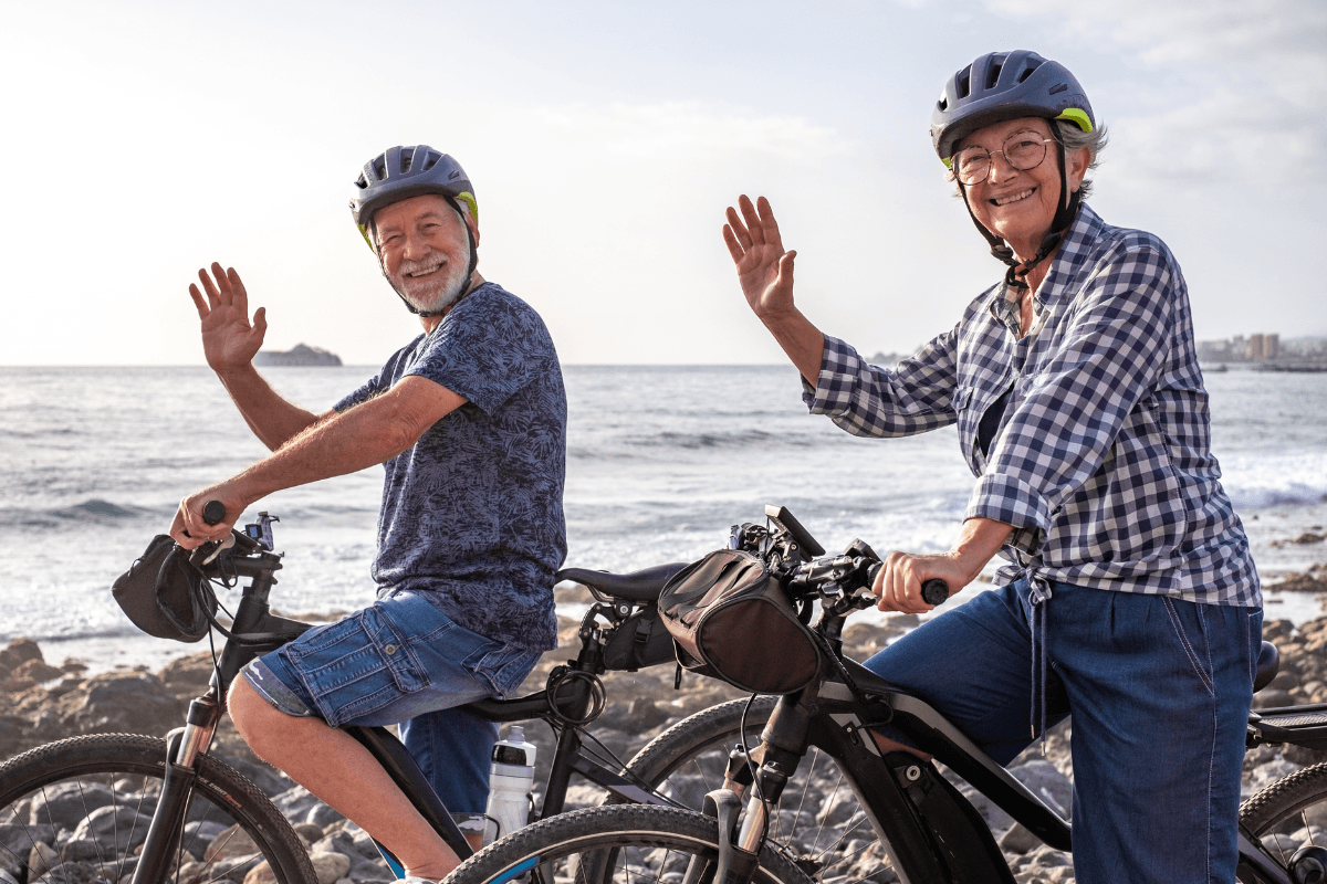 Senior couple cycling by ocean, waving