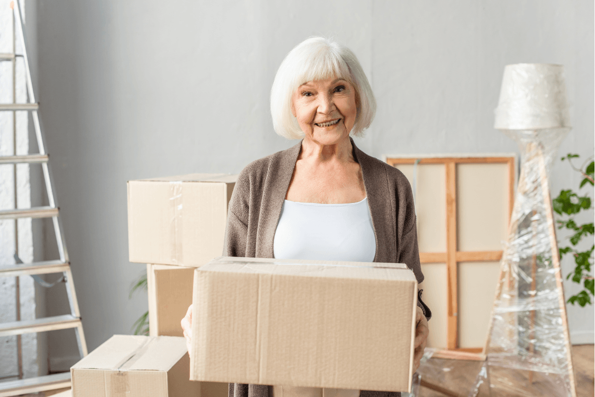 Smiling senior woman holding moving box indoors