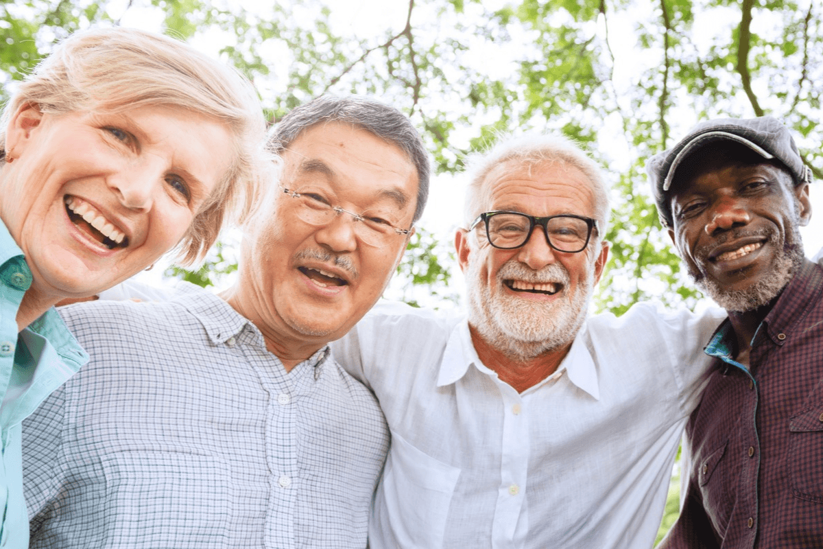 Four smiling older friends outdoors, posing closely together.