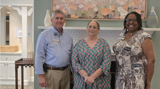 Three smiling adults standing indoors before wall art