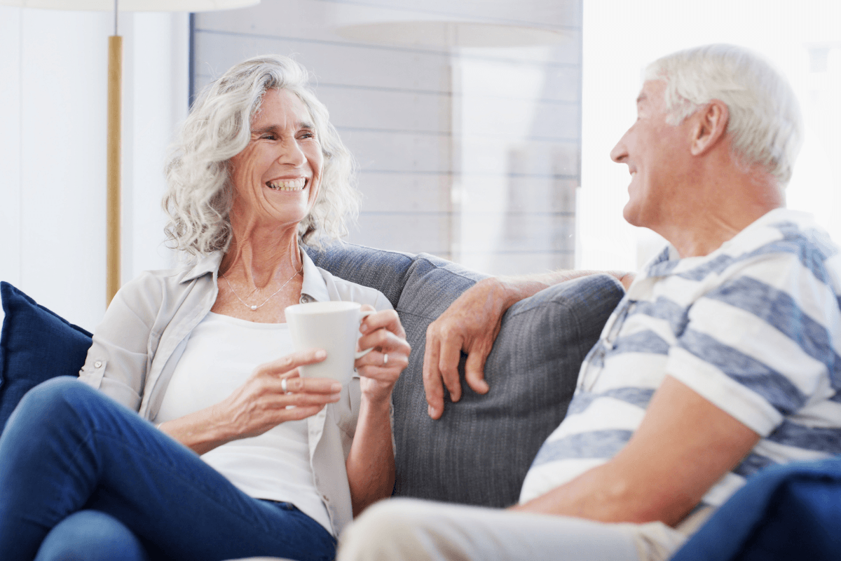 Smiling senior couple chatting on couch with coffee