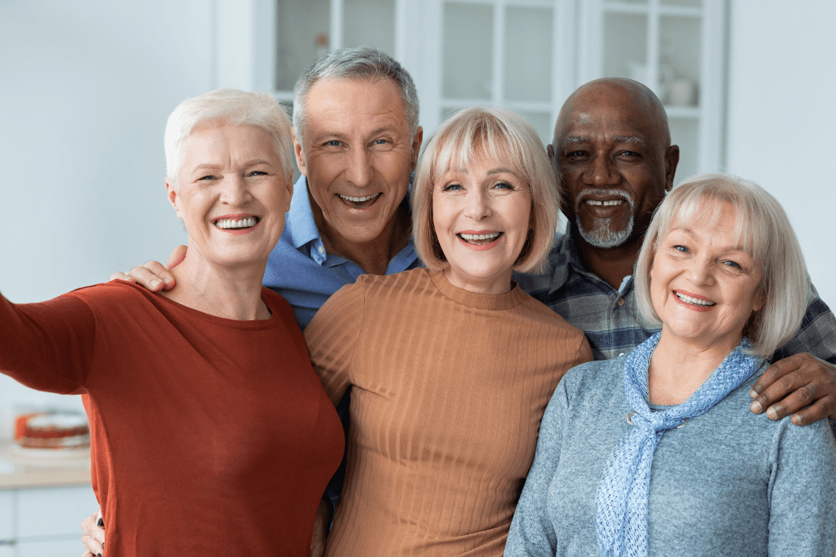 Five smiling seniors taking a group selfie indoors