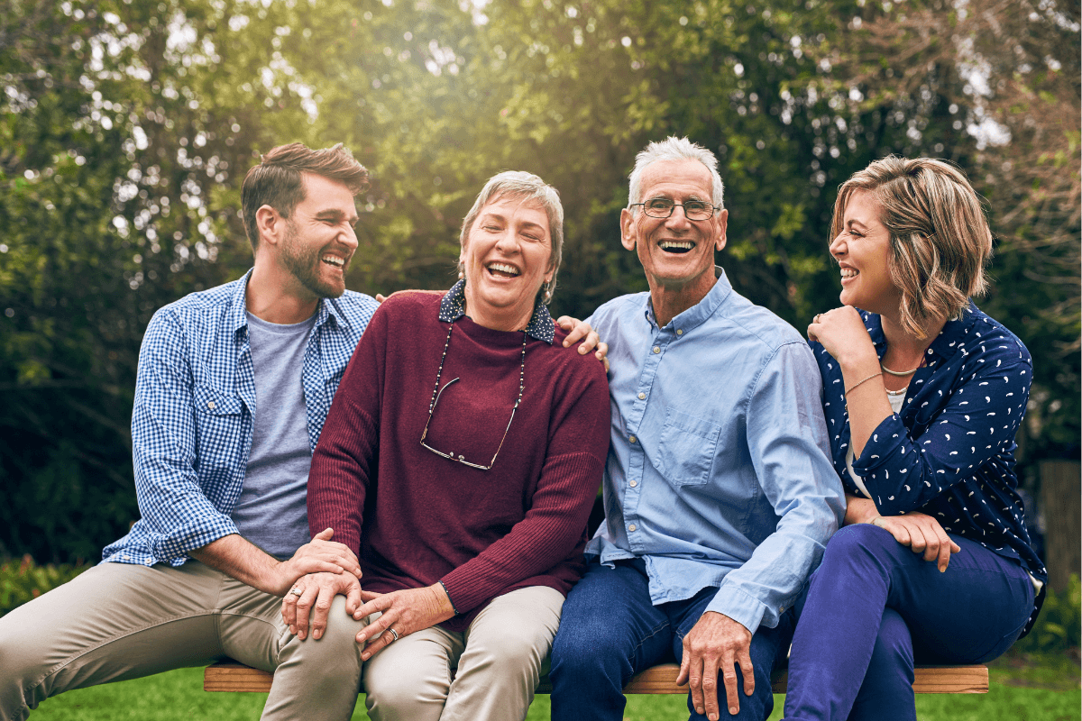 Four adults laughing together on outdoor bench