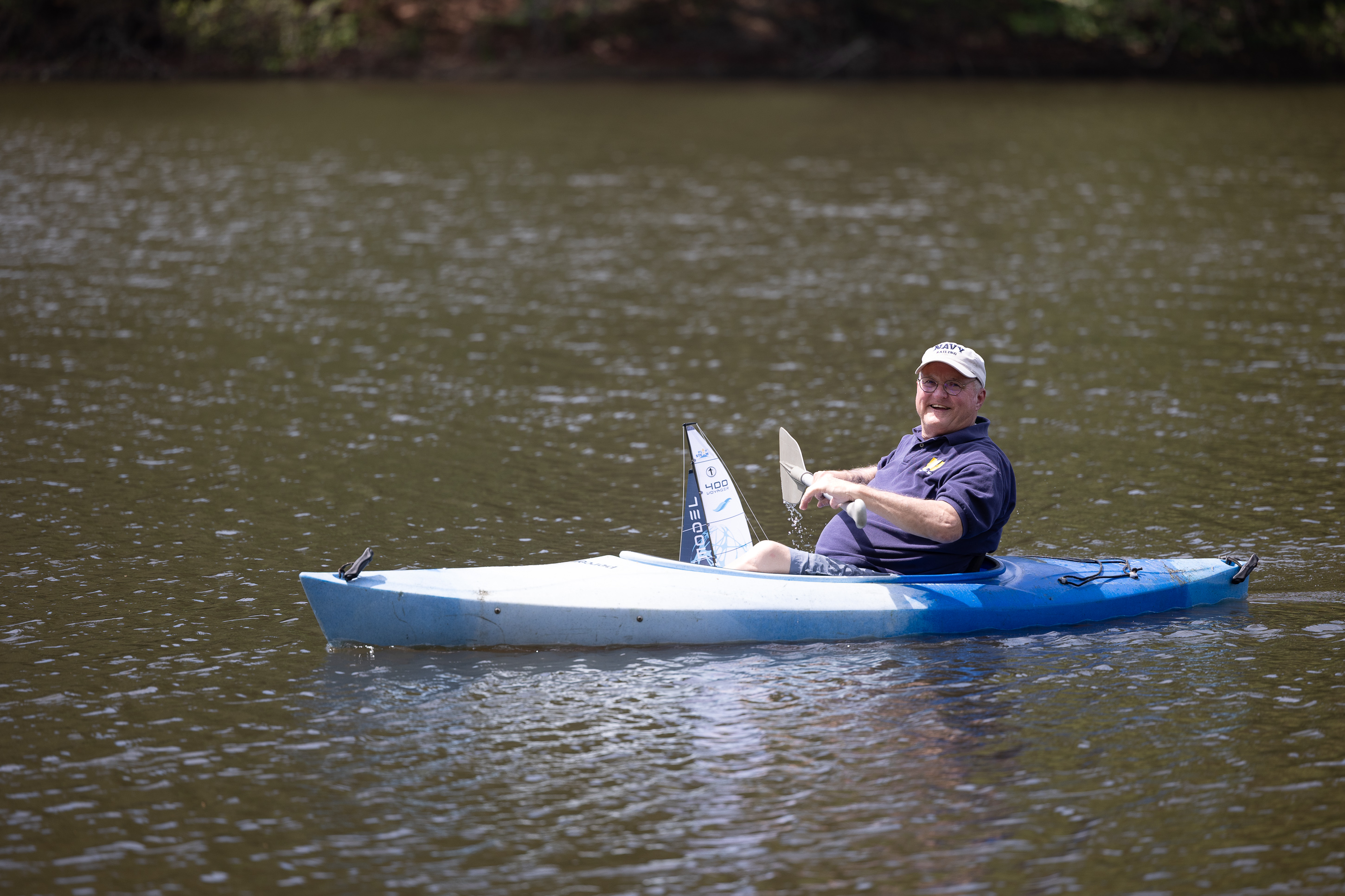 Man in kayak holding model sailboat on lake