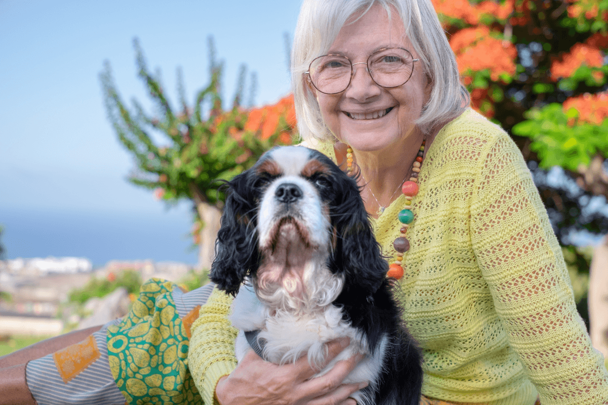 Smiling elderly woman holds black-and-white spaniel outdoors.