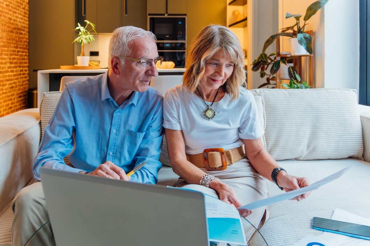 Senior couple actively managing household finances and retirement savings, using laptop and documents to review bills, budget, insurance, and investment planning at home