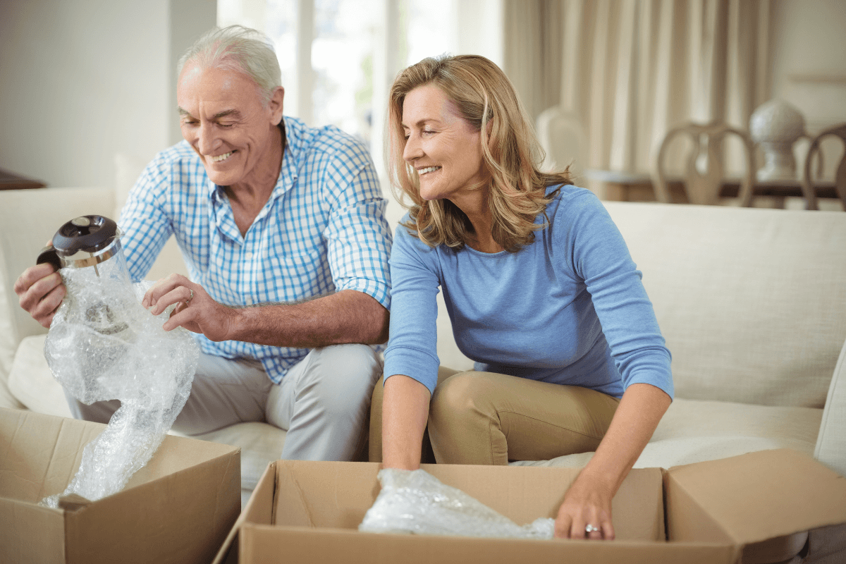 Smiling older couple unpacking kitchen items in new home.