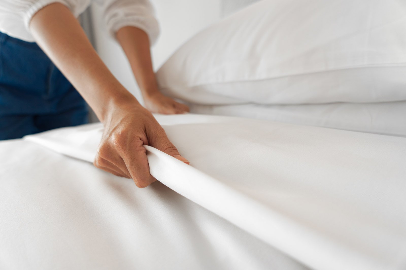 Person tucking white sheet onto mattress