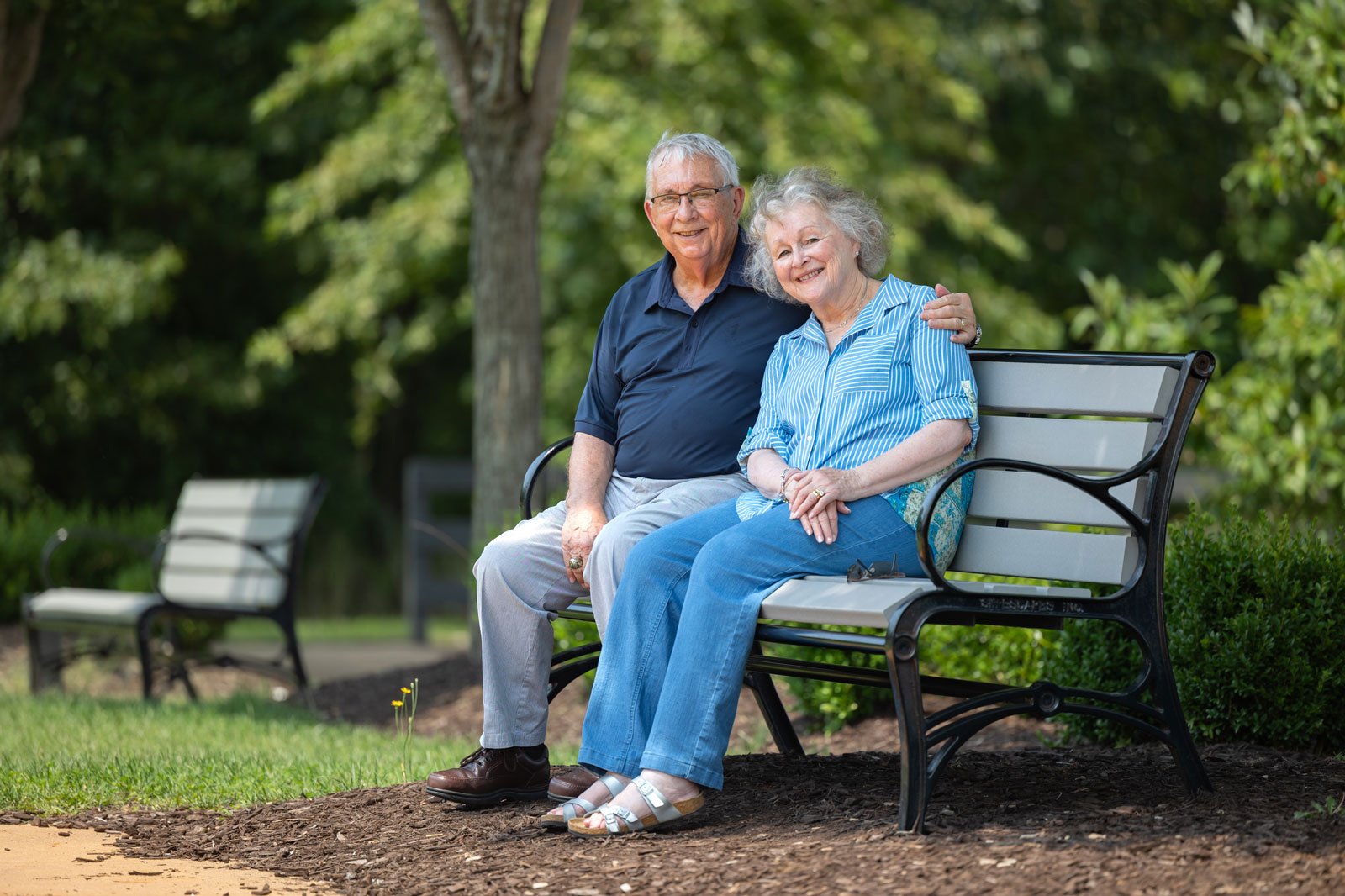 Elderly couple sitting on park bench smiling