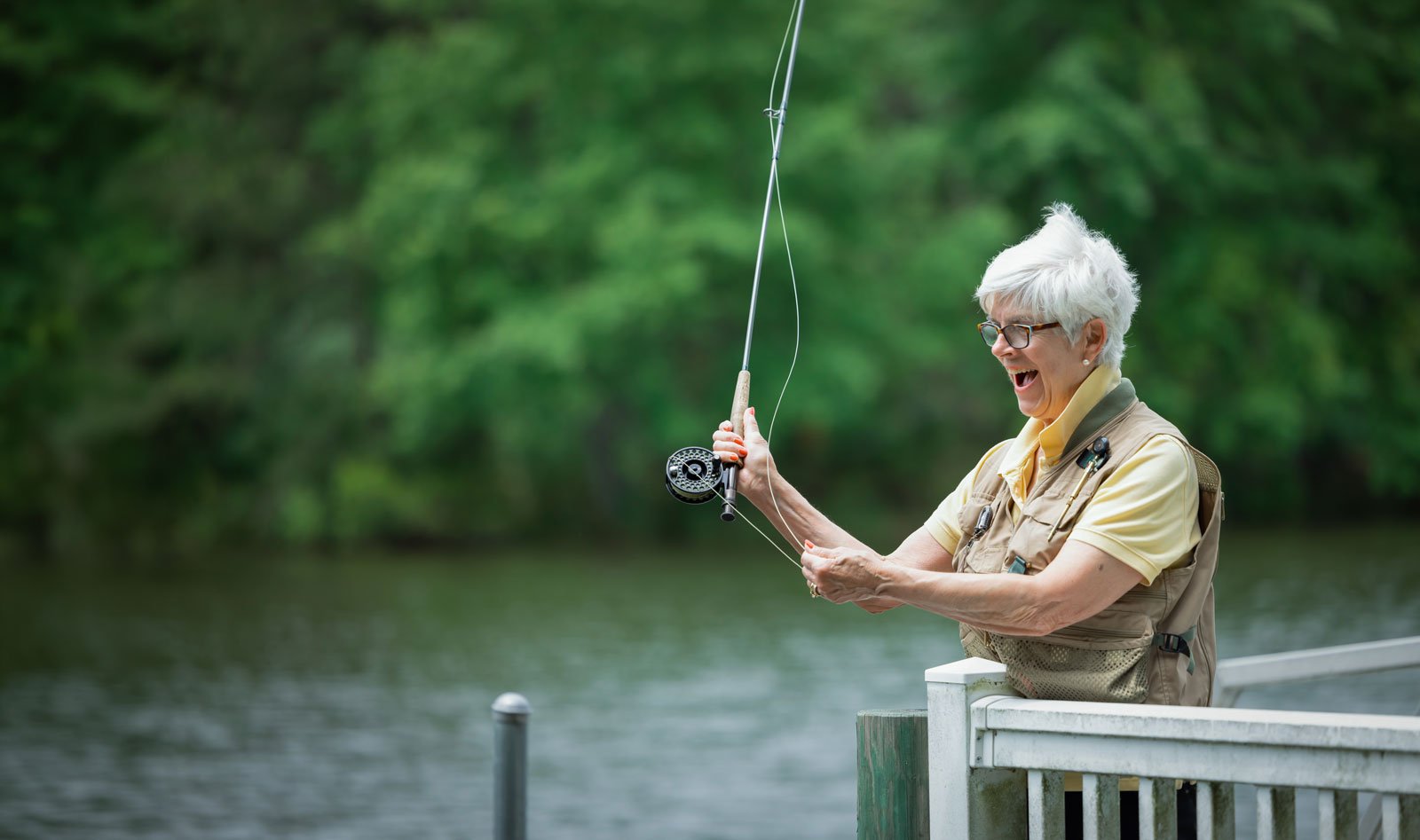 Senior woman fly fishing on lakeside dock