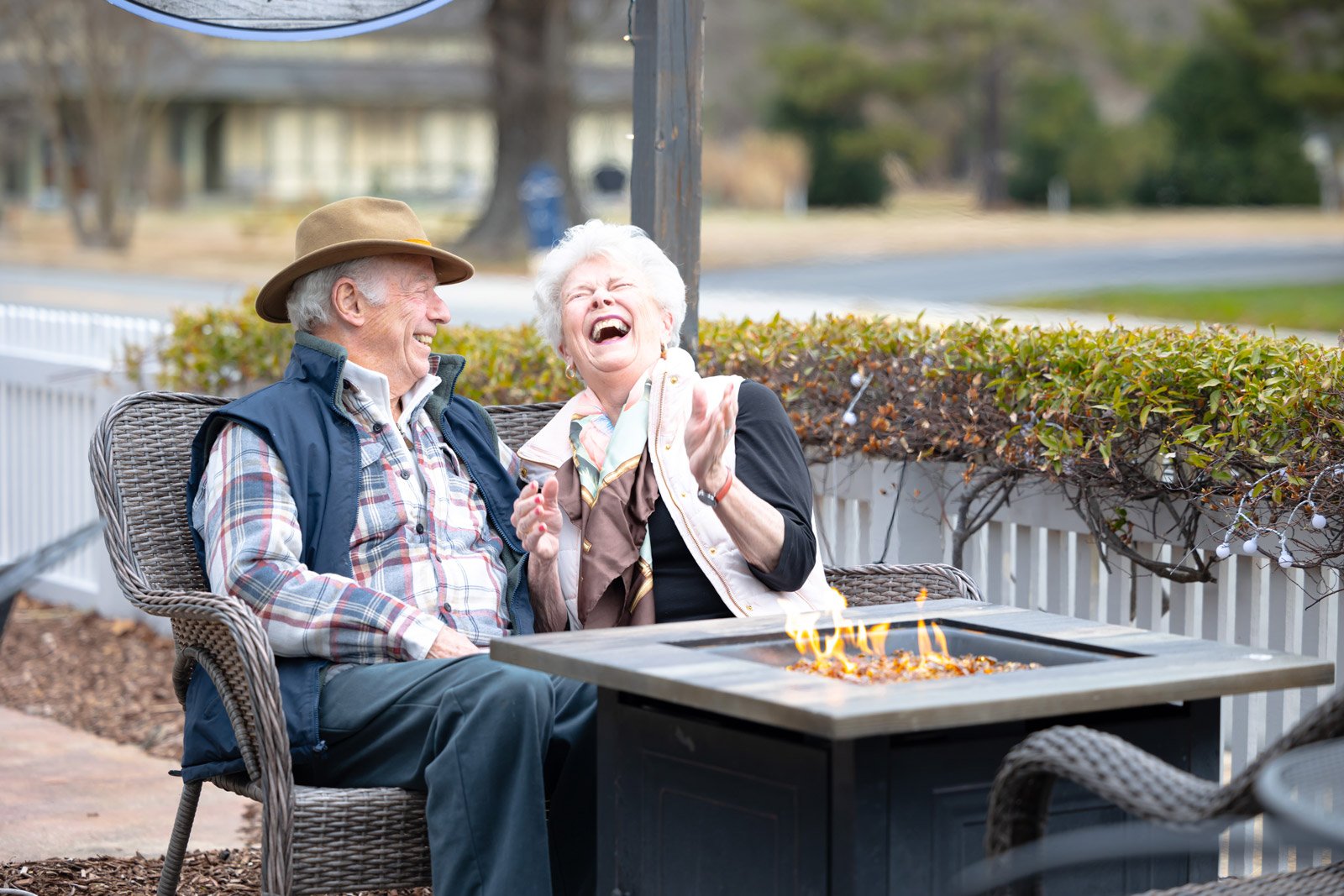 Elderly couple laughing by outdoor fire pit table