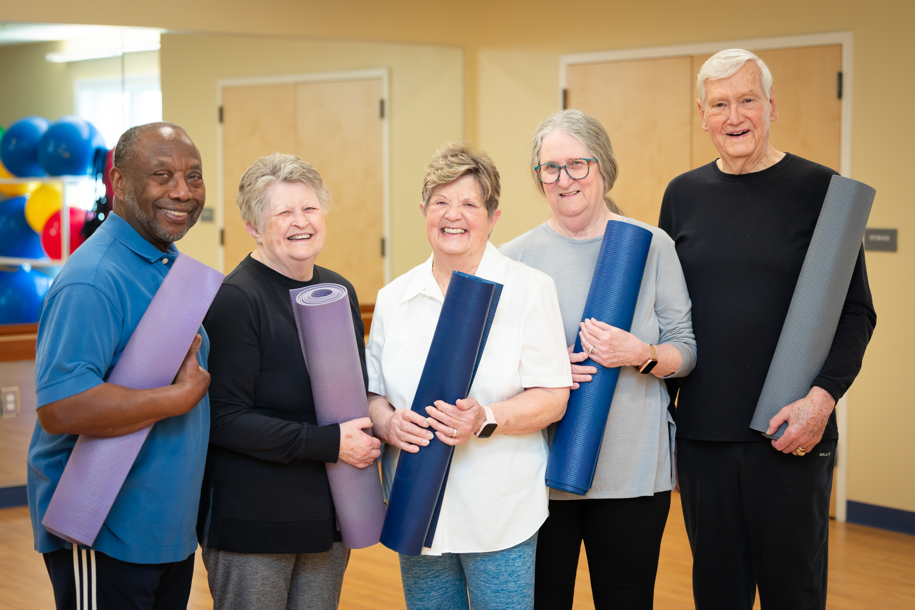 Five seniors holding yoga mats in fitness studio