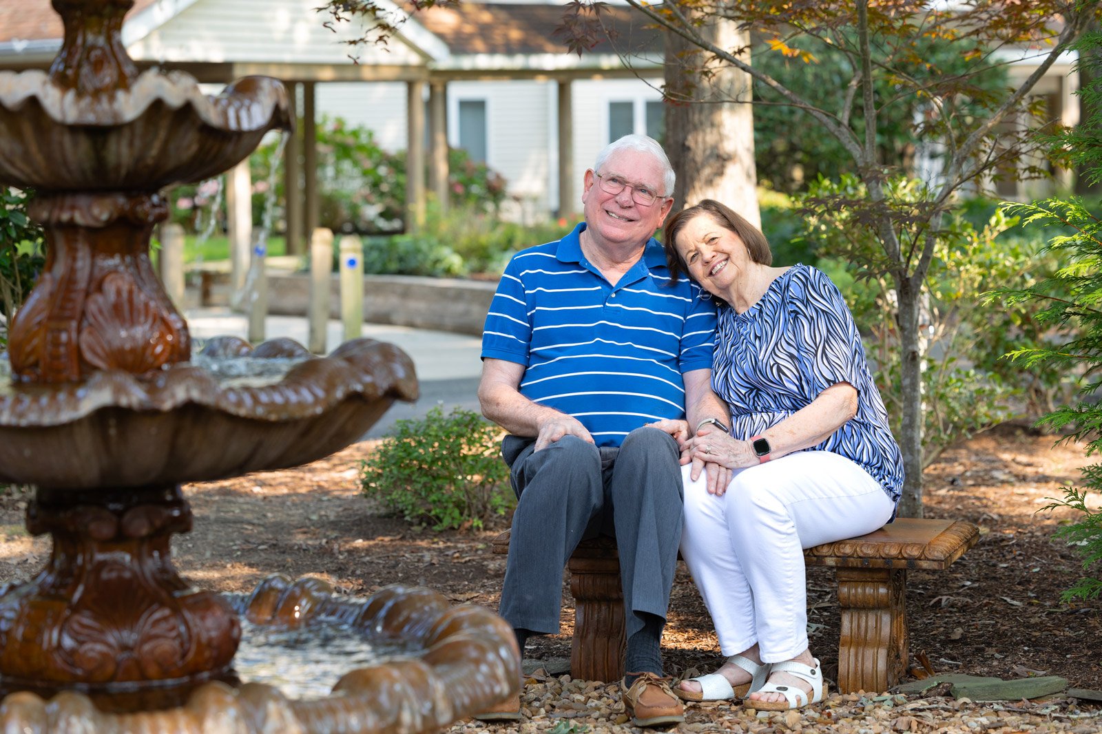 Elderly couple sitting on bench by garden fountain