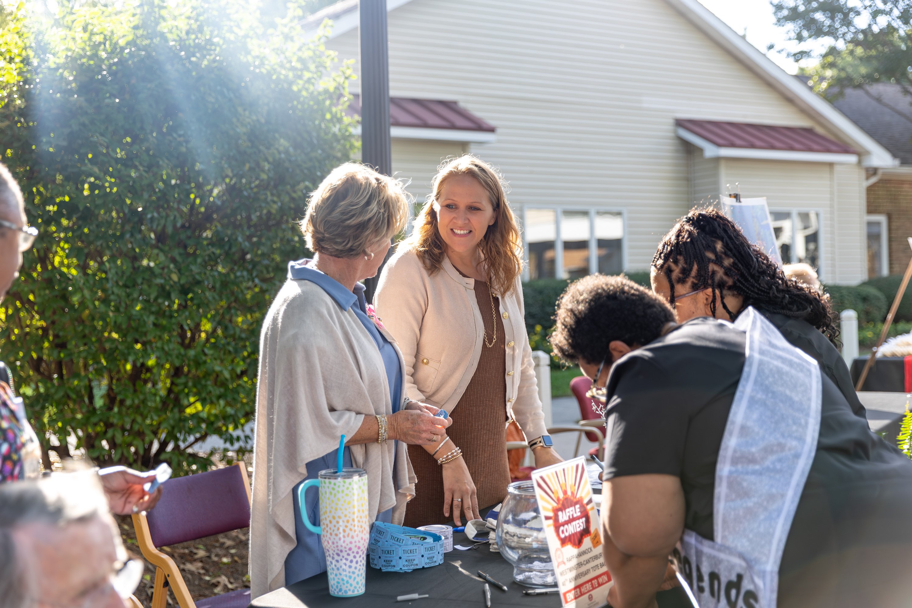 Women at outdoor raffle table in sunlight