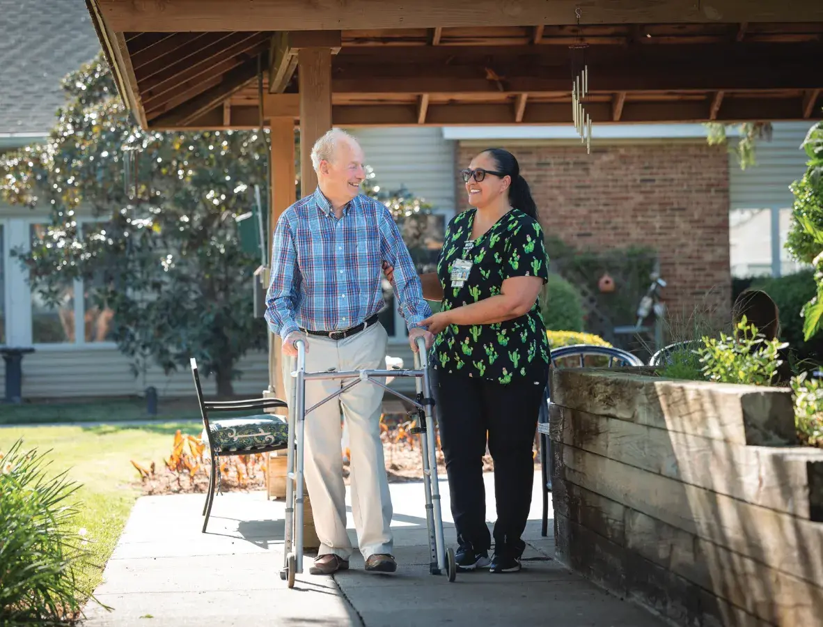 Caregiver walks beside senior man using a walker
