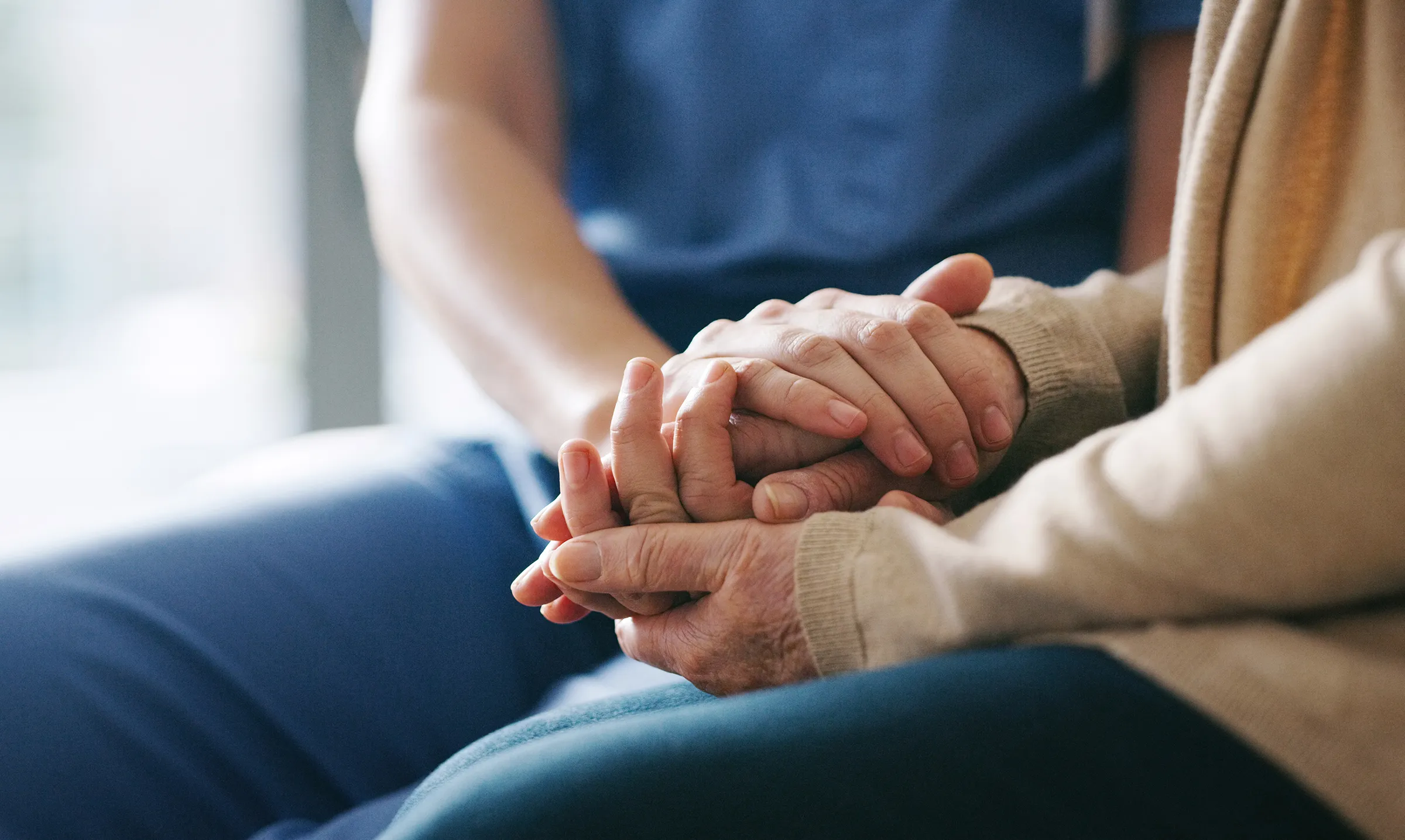 Caregiver holding elderly person's hands in support