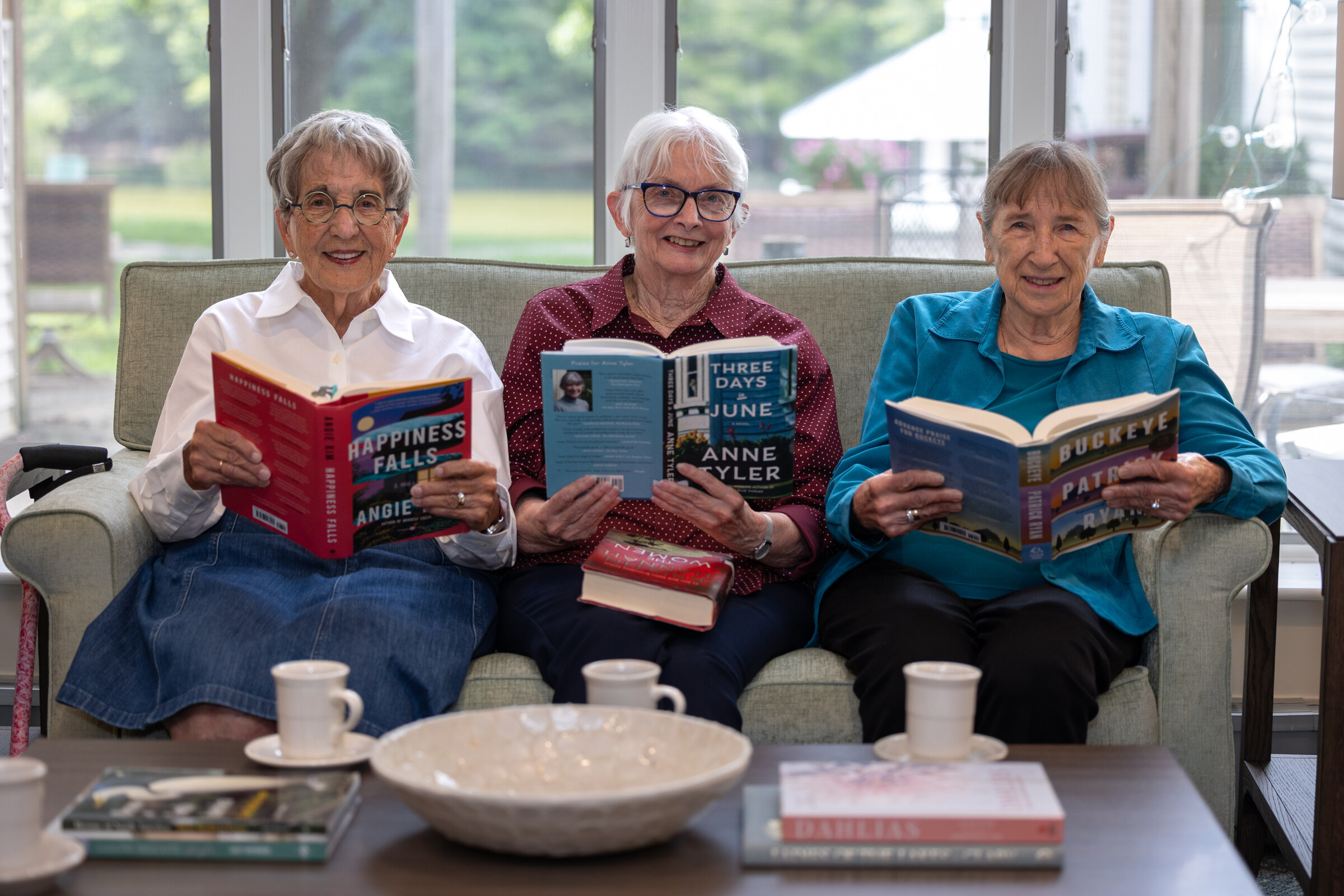 Three elderly women reading books on a couch