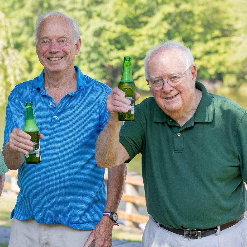 Two elderly men toasting with beer bottles outdoors