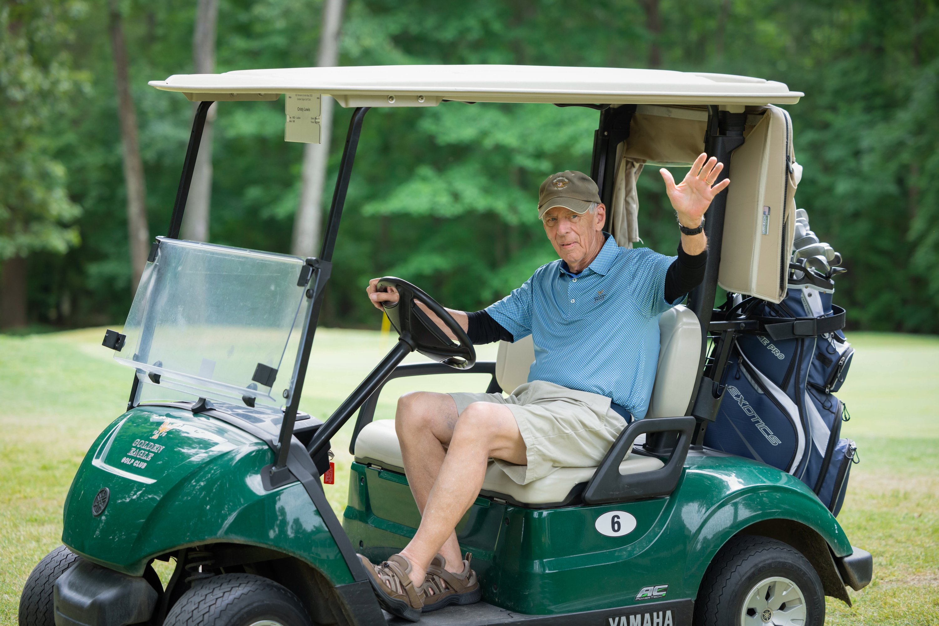 Man waving while driving golf cart on course