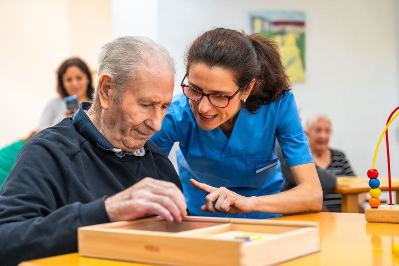 Caregiver assisting elderly man with tabletop activity